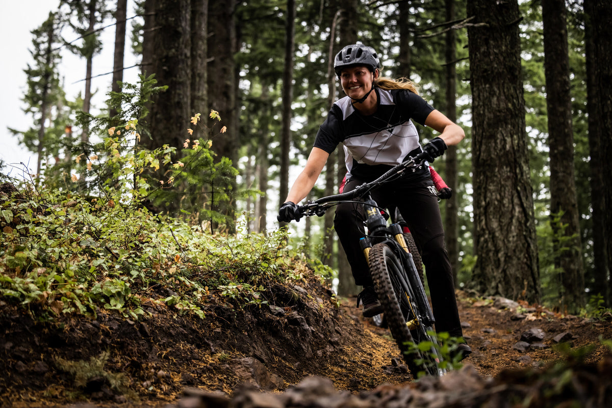 Woman riding in the Black/White FLOW short sleeve jersey on a wooded trail